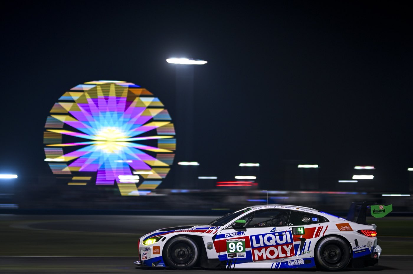The #96 Turner Motorsport BMW M4 GT3 EVO at night past the Daytona ferris wheel